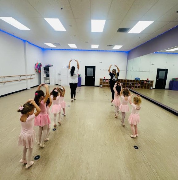 young dance students in leotards and skirts practicing ballet with their dance teachers